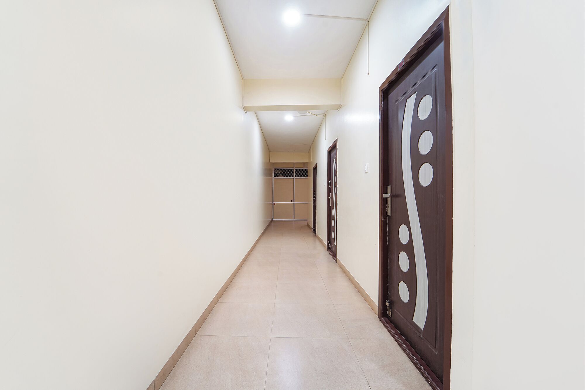 A corridor with a tiled floor, a door with circular cutouts, and a ceiling light fixture.