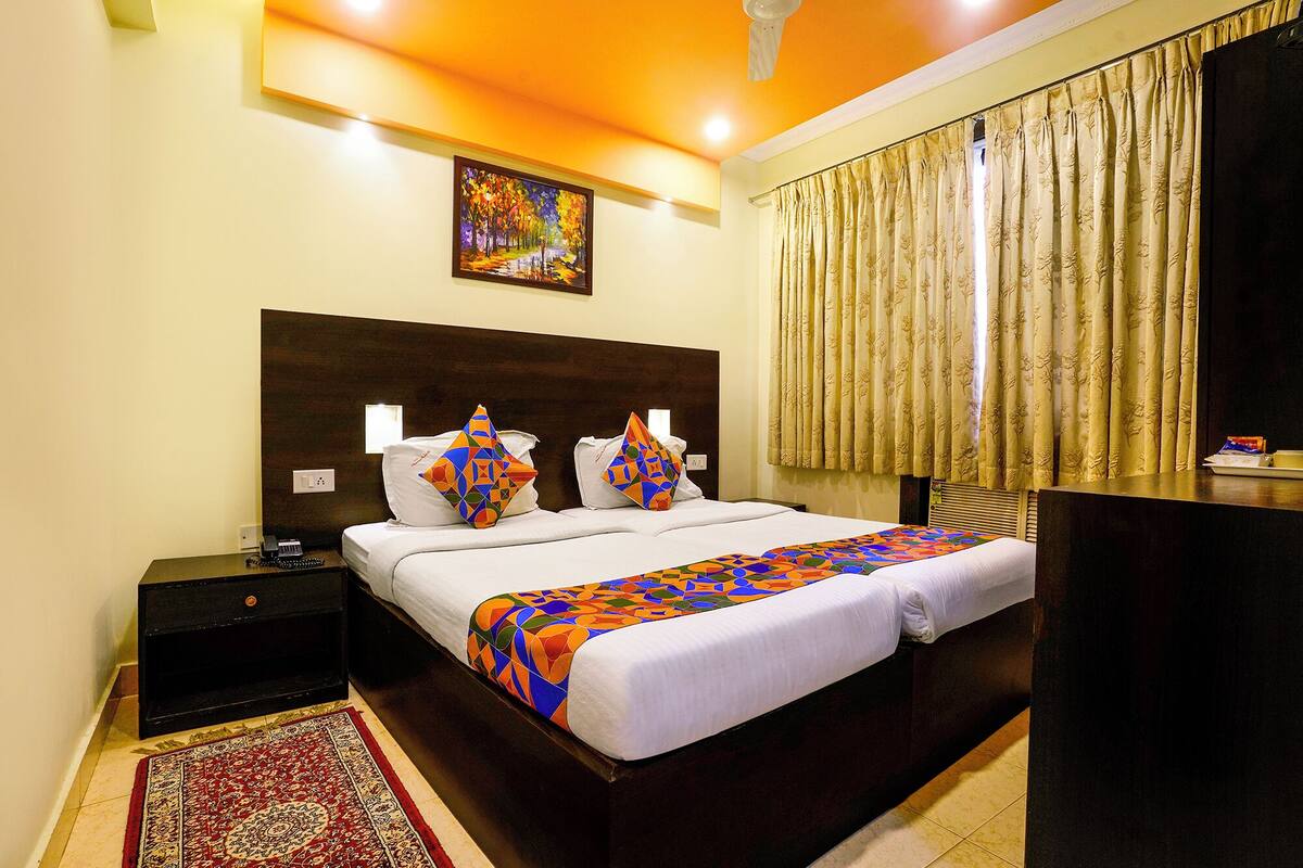 A hotel room with a large bed, a nightstand, a desk, a patterned rug, and a painting on the wall.