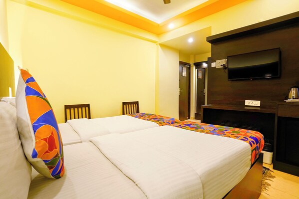 A hotel room with two beds, a TV mounted on the wall, and a desk with a chair. - FabHotel Manoshanti - Nr. Big Daddy Casino (Panaji)
