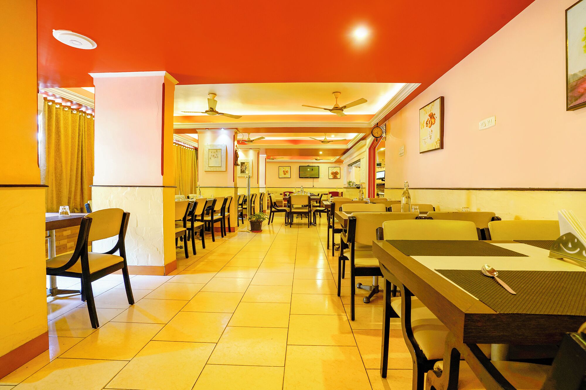 A restaurant with multiple dining tables and chairs, ceiling fans, and wall-mounted televisions.