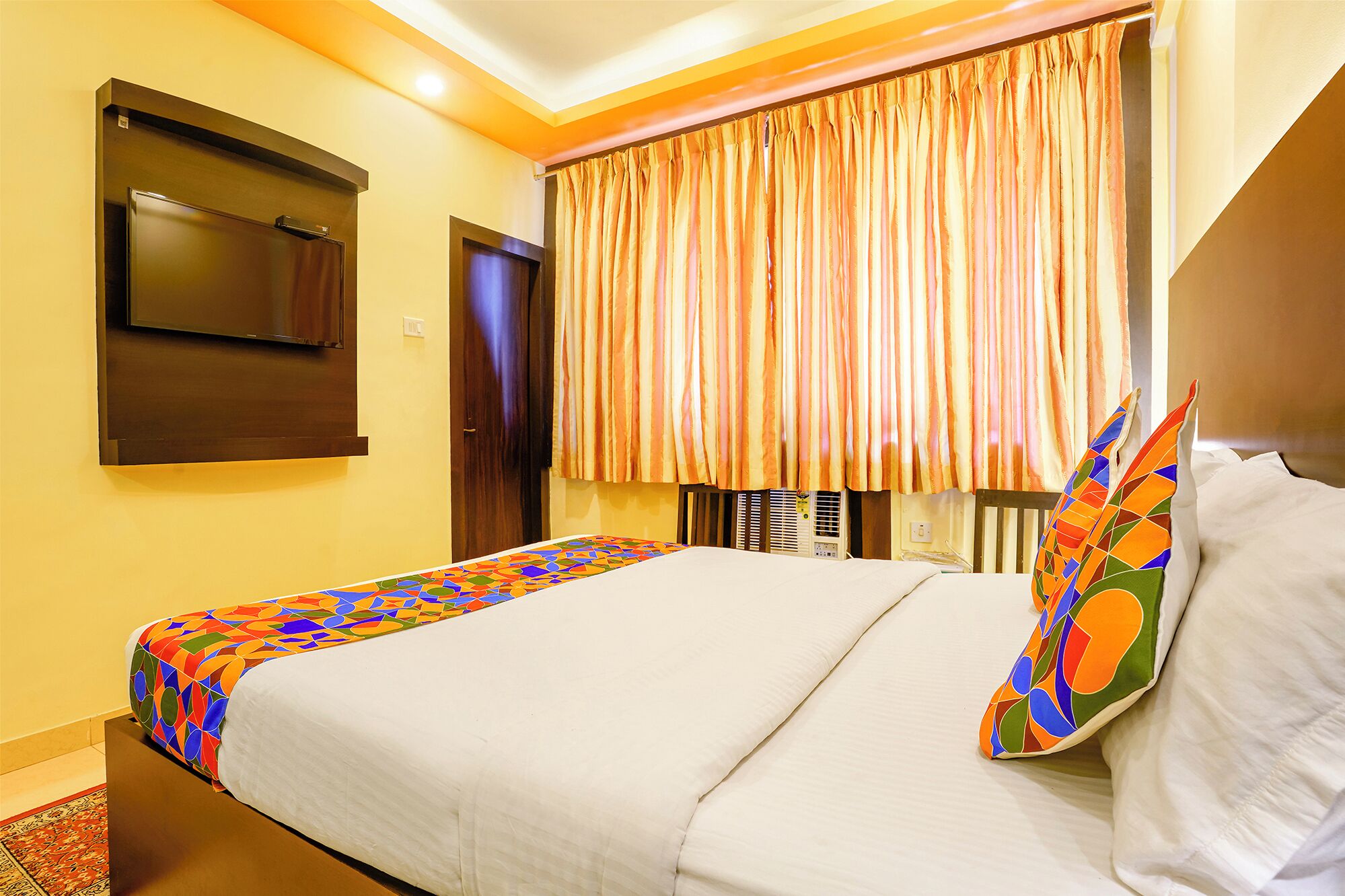 A hotel room with a bed, a television mounted on the wall, and a window with curtains.