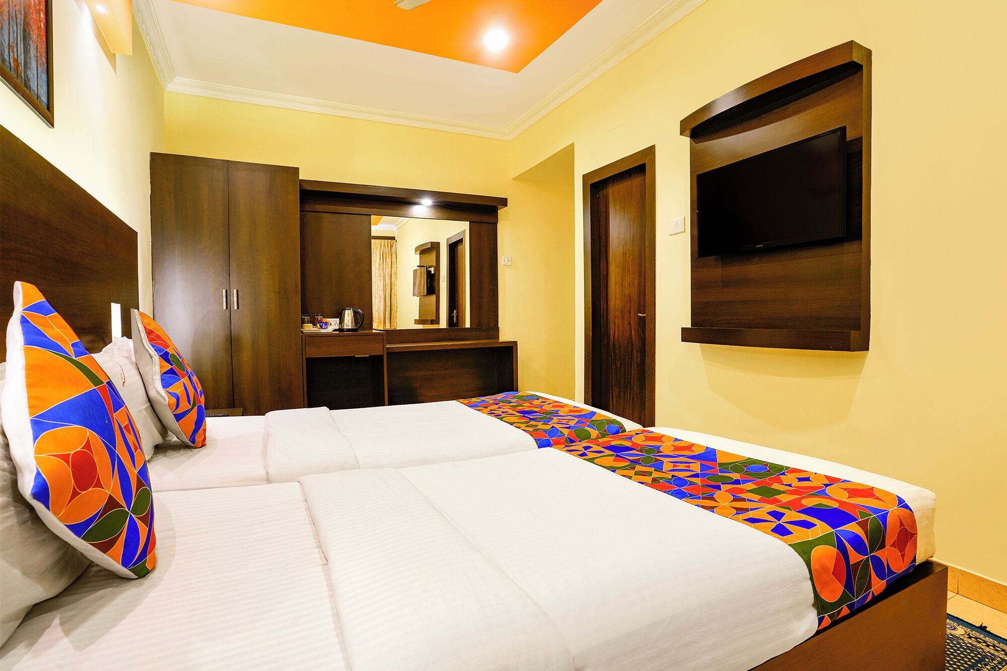 A hotel room with two beds, a large mirror, a flat-screen TV, and a wooden wardrobe.