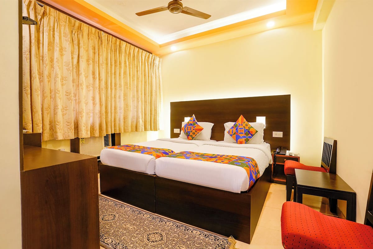 A hotel room with a bed, a desk, a chair, a bedside table, and a ceiling fan.