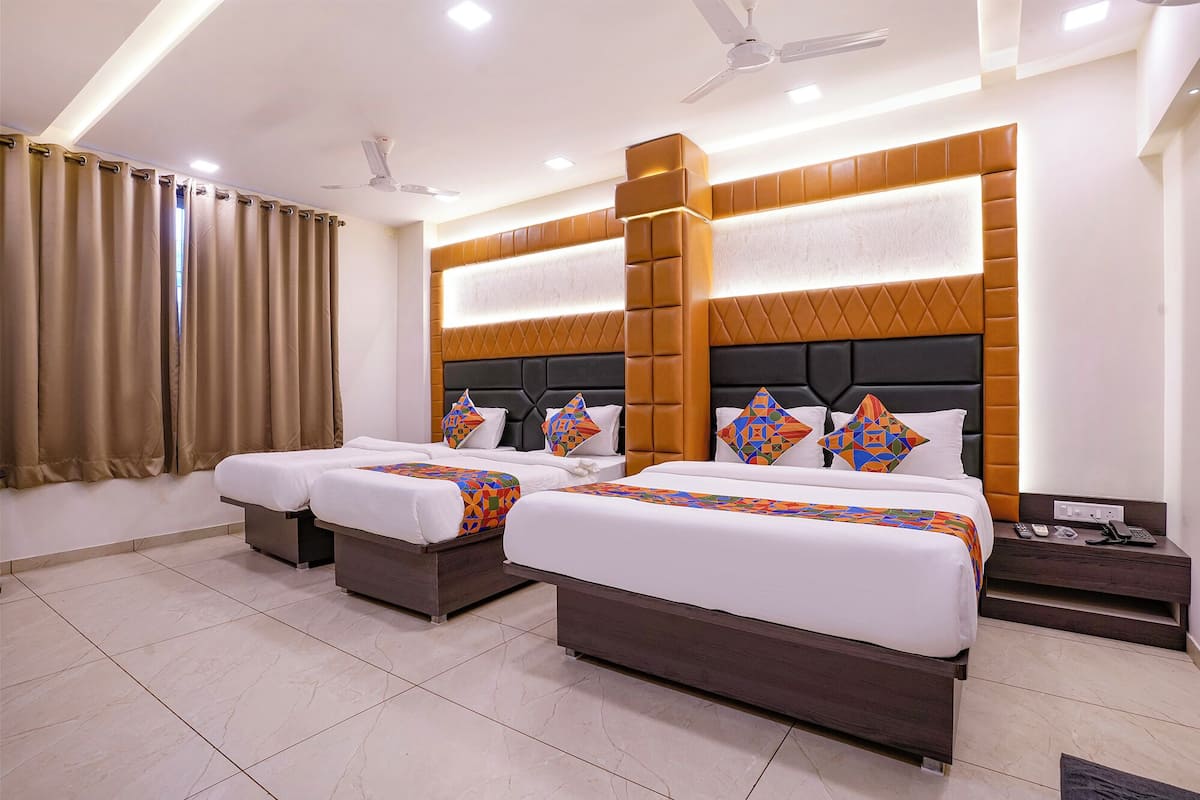 Quarto de hotel com duas camas, uma janela grande com cortinas, um ventilador de teto e uma mesinha de cabeceira com telefone e carregador.