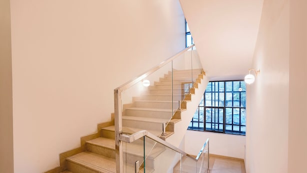 A modern staircase with glass railings and a view of the outside through a large window. - Fabhotel Sunshine Residency (Navi Mumbai)
