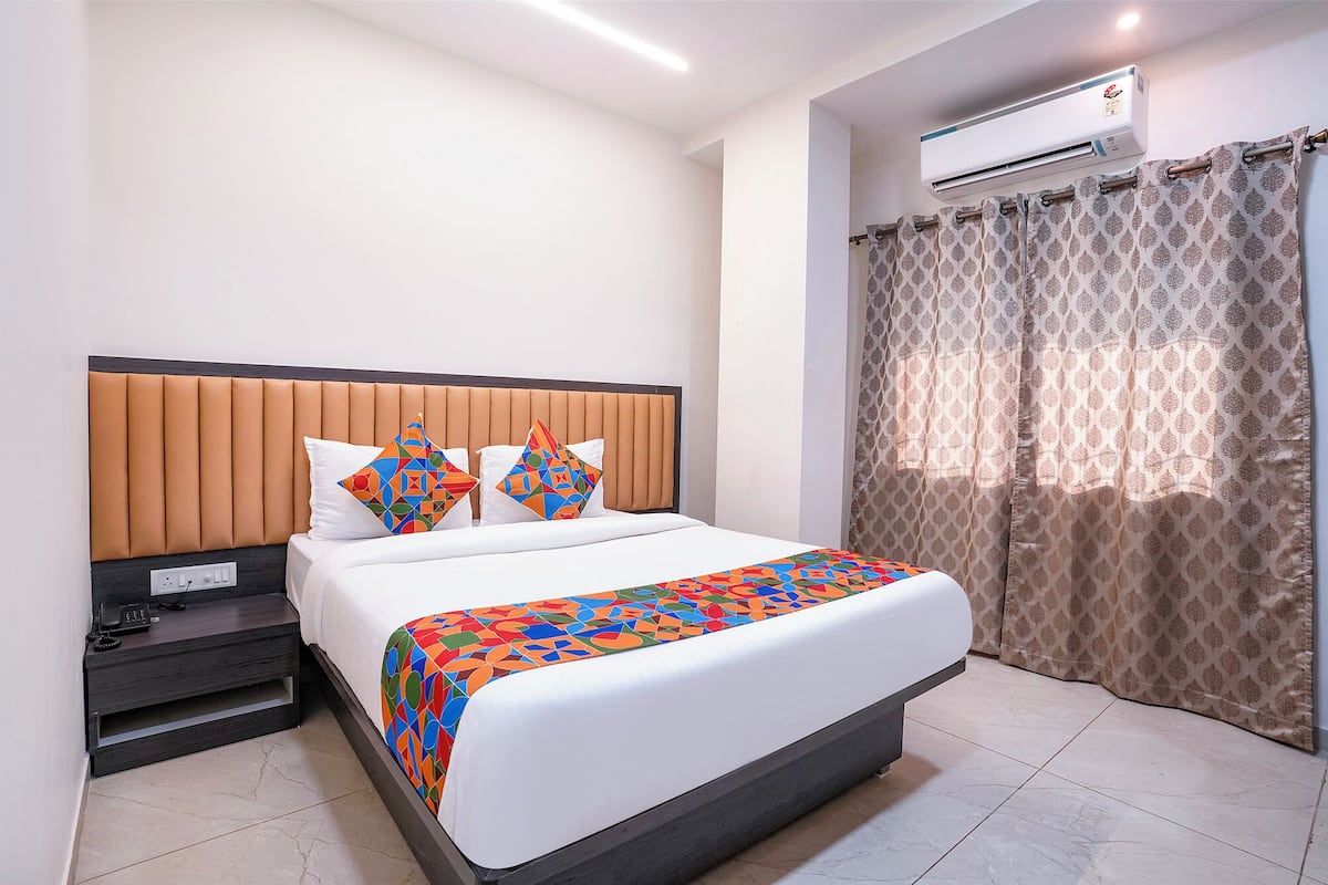 Quarto de hotel com cama, mesa de cabeceira com telefone, ar condicionado e cortinas estampadas.