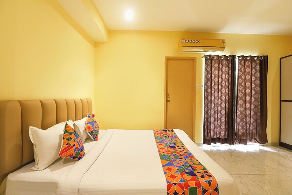A hotel room with a bed, a window with curtains, an air conditioning unit, and a door.