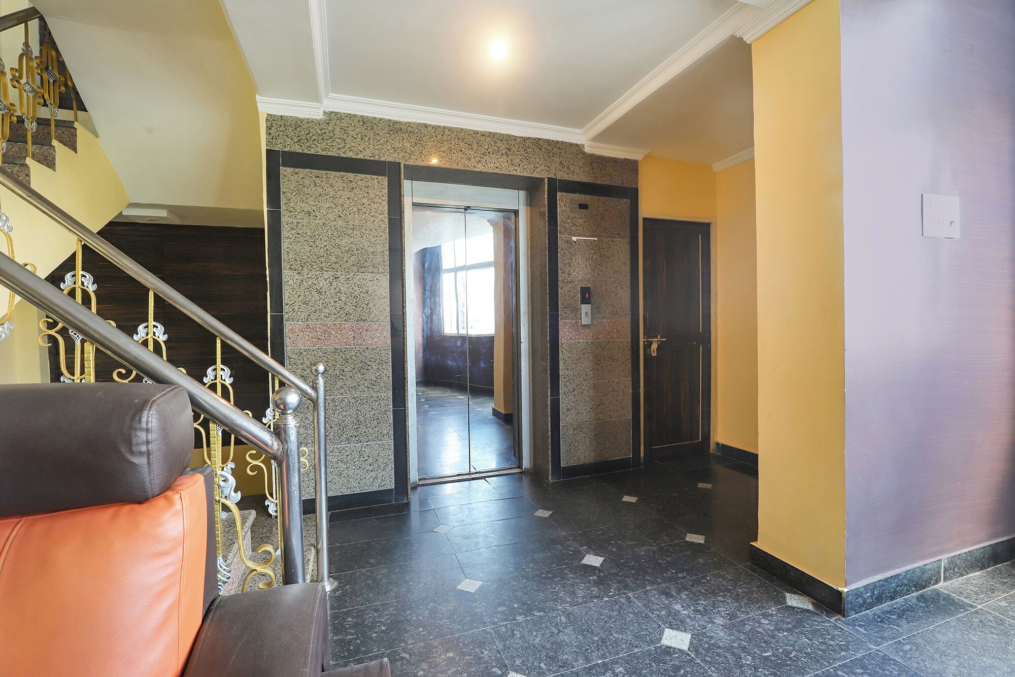 A hotel lobby with a marble floor, a staircase with metal railings, and a door with a number plate.