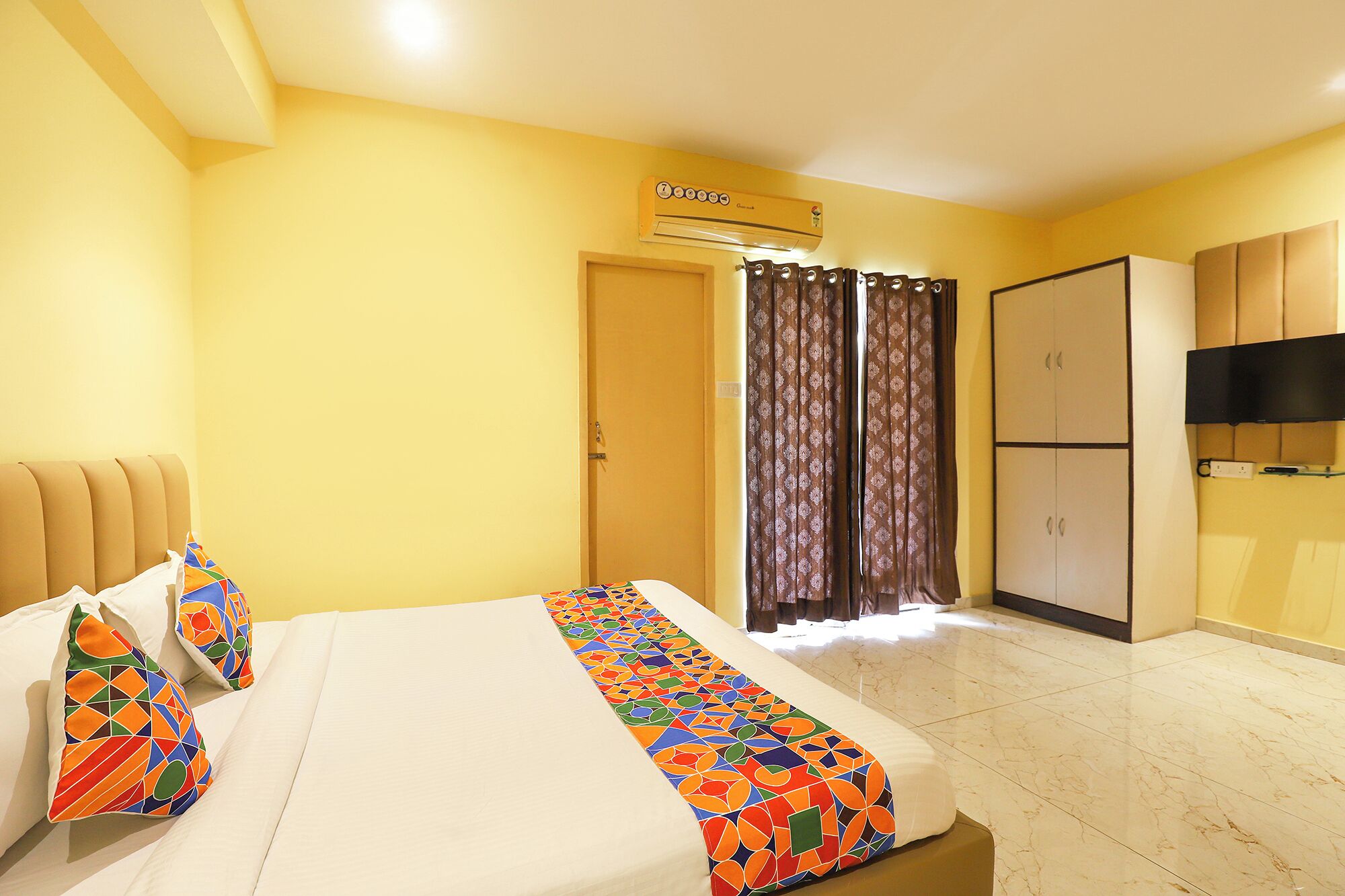 A hotel room with a bed, a wardrobe, a television, and an air conditioning unit.