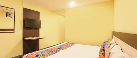A hotel room with a bed, a TV mounted on the wall, a ceiling fan, and a small shelf.