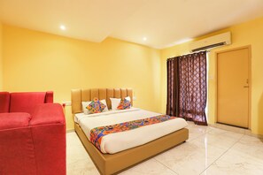 Quarto de hotel com uma cama, uma cadeira vermelha, cabeceira marrom e edredom estampado, além de uma cortina.