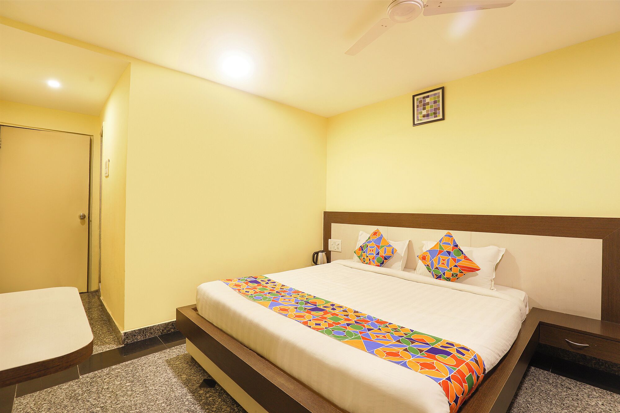 A hotel room with a bed, a bedside table, a chair, and a ceiling fan.