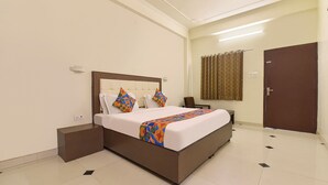 Una habitación de hotel con una cama grande, una mesita de noche, una silla, una puerta y una cortina.