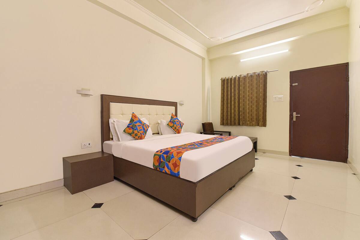 Een hotelkamer met een groot bed, een nachtkastje, een stoel, een deur en een gordijn.