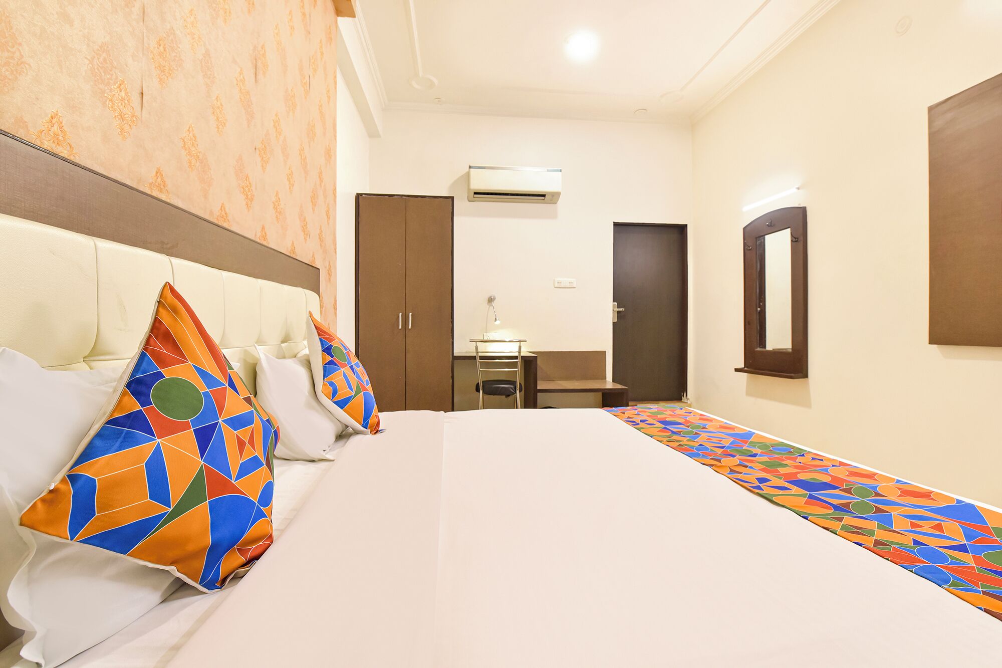 A hotel room with a large bed, a desk, an air conditioning unit, and a mirror on the wall.