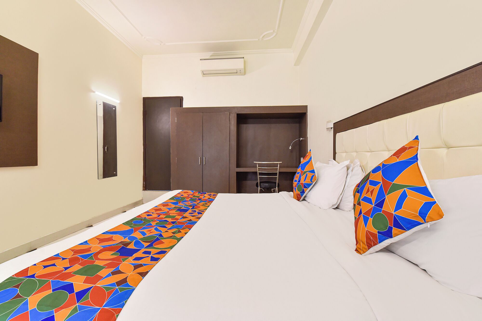 A hotel room with a bed, a wardrobe, and a small table with a chair.