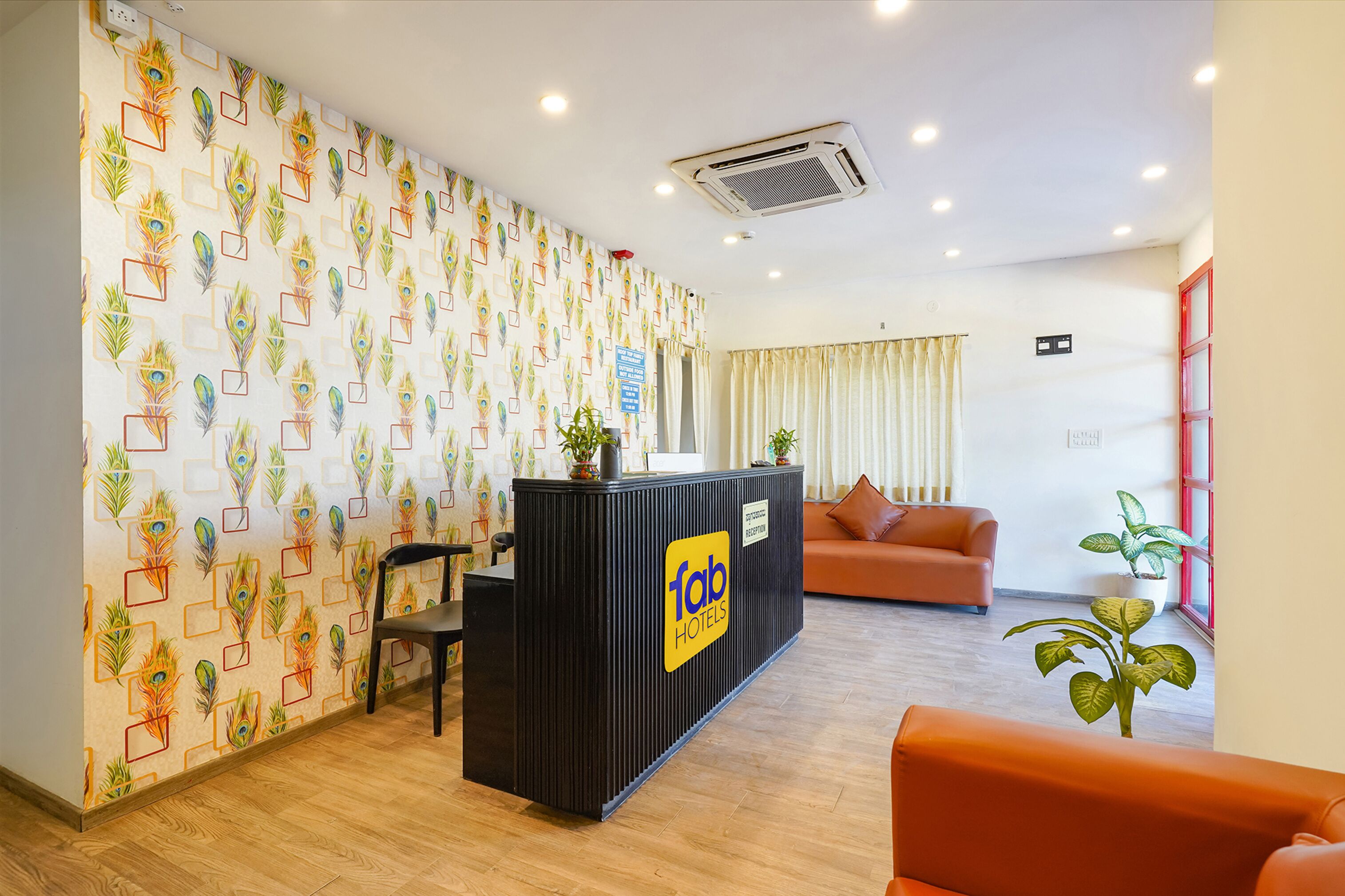 A reception desk with a 'fab hotels' sign, a wooden floor, an orange sofa, and a patterned wall.