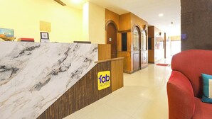 Zona de recepción de hotel con mostrador de mármol, escritorio de madera y un sofá rojo.