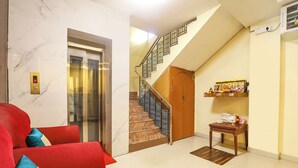 Un vestíbulo de hotel con pared de mármol, un sofá rojo, una escalera y una pequeña mesa de madera con un objeto decorativo.