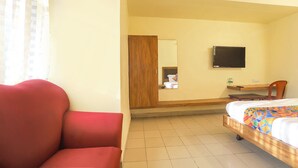 Una habitación de hotel con una cama, un escritorio de madera, una silla, un televisor y un espejo.