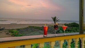 Un balcón con dos bebidas y vista a la playa.