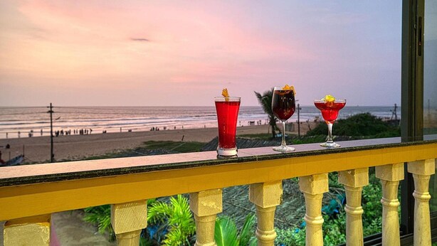 Un balcón con tres bebidas y vista a la playa.