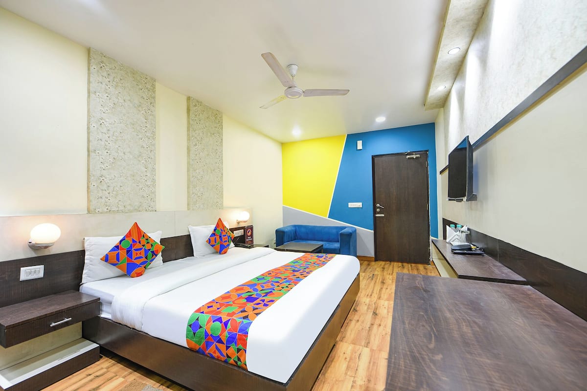 Habitación de hotel con cama, mesitas de noche, escritorio, silla, ventilador de techo y una puerta.