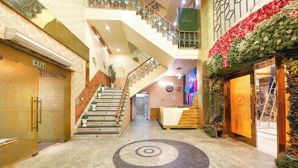 Un vestíbulo de hotel con una escalera central, una recepción y una pared decorativa con flores.