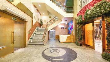 A hotel lobby with a central staircase, a reception desk, and a decorative wall with flowers.