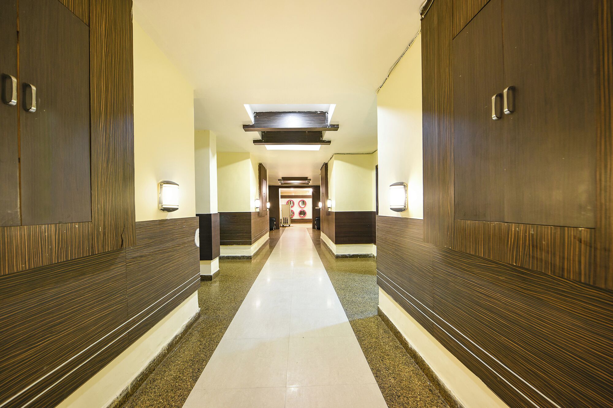 Corredor de hotel com painéis de madeira, luminária central e piso ladrilhado.