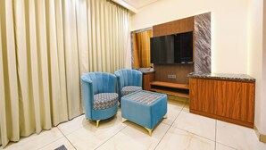Una sala de estar moderna con dos sillones azules, un reposapiés estampado, un mueble de madera y un televisor de pantalla plana montado en una pared de mármol.