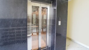 An elevator with a glass door, a control panel with a button, and a marble floor. - Fabhotel Radhika Palace (Faizabad)