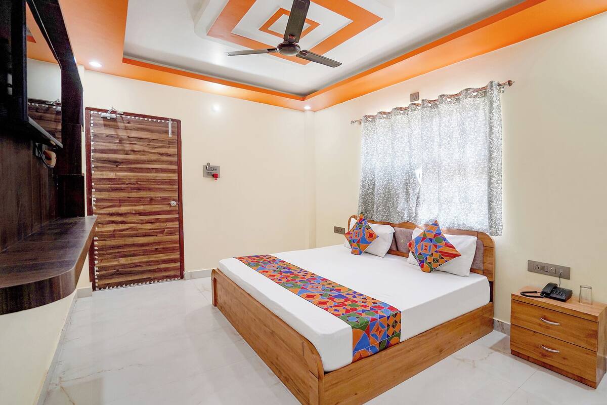 A bedroom with a wooden bed, a nightstand, a ceiling fan, and a window with lace curtains.