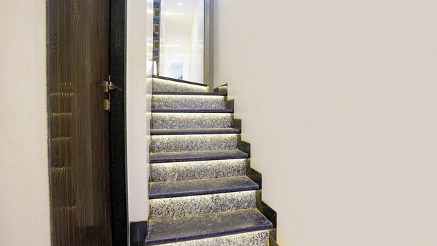 A staircase with a dark wooden door and a light-colored wall. - Fabexpress Rose Inn (Mumbai)
