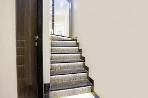 A staircase with a dark wooden door and a light-colored wall. - Fabexpress Rose Inn (Mumbai)