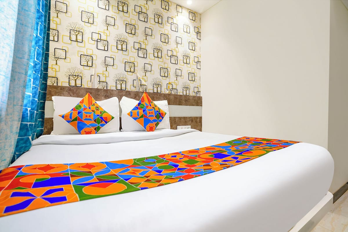 A hotel room with a large bed, a patterned wall, and a colorful bedspread.