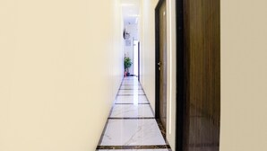 A hallway with a marble floor, a wooden door on the right, and a potted plant in the distance. - Fabexpress Rose Inn (Mumbai)