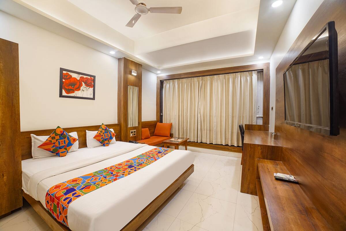 Une chambre d’hôtel avec un grand lit, un bureau, une chaise, un ventilateur de plafond, une fenêtre avec des rideaux et un tableau au mur.