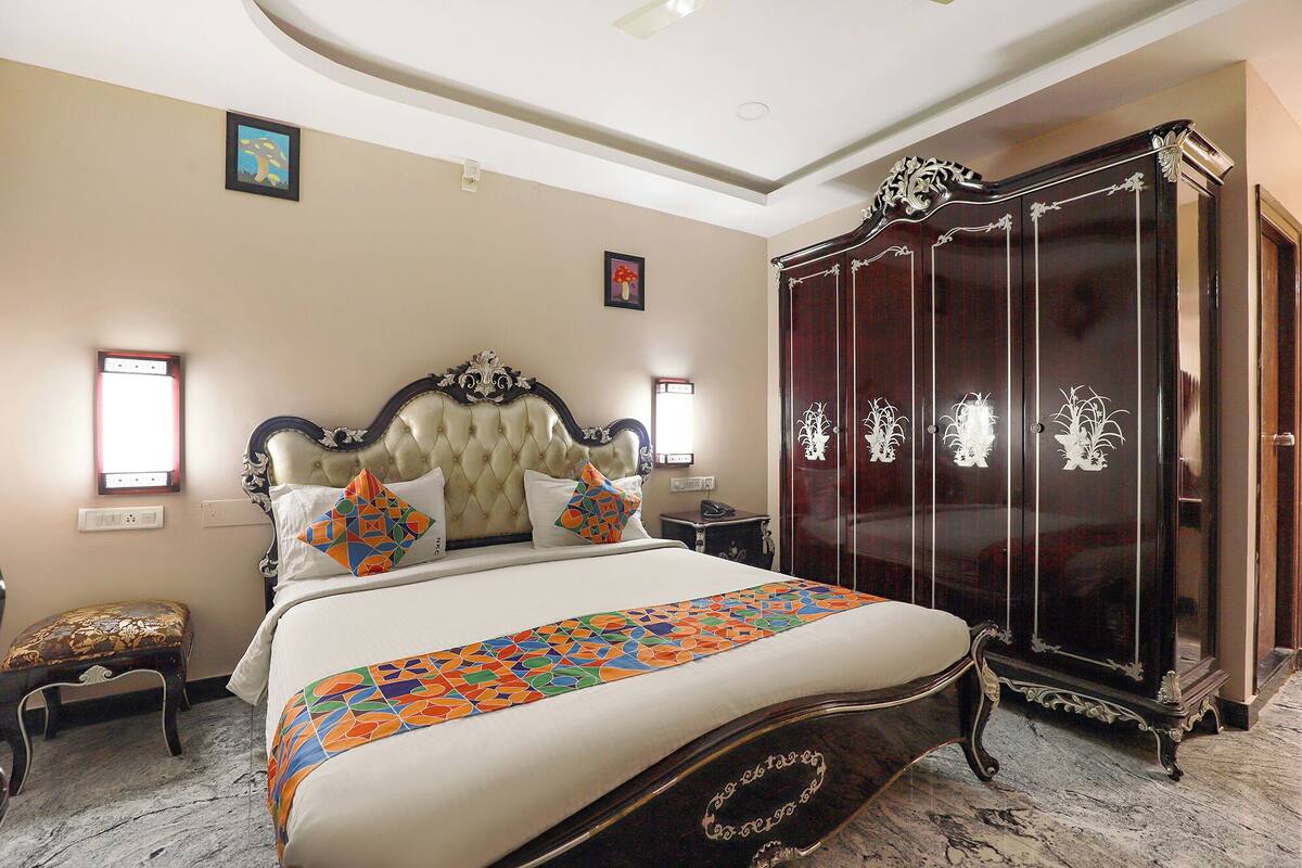 A bedroom with a large bed, a dark wooden wardrobe, and a small bedside table.