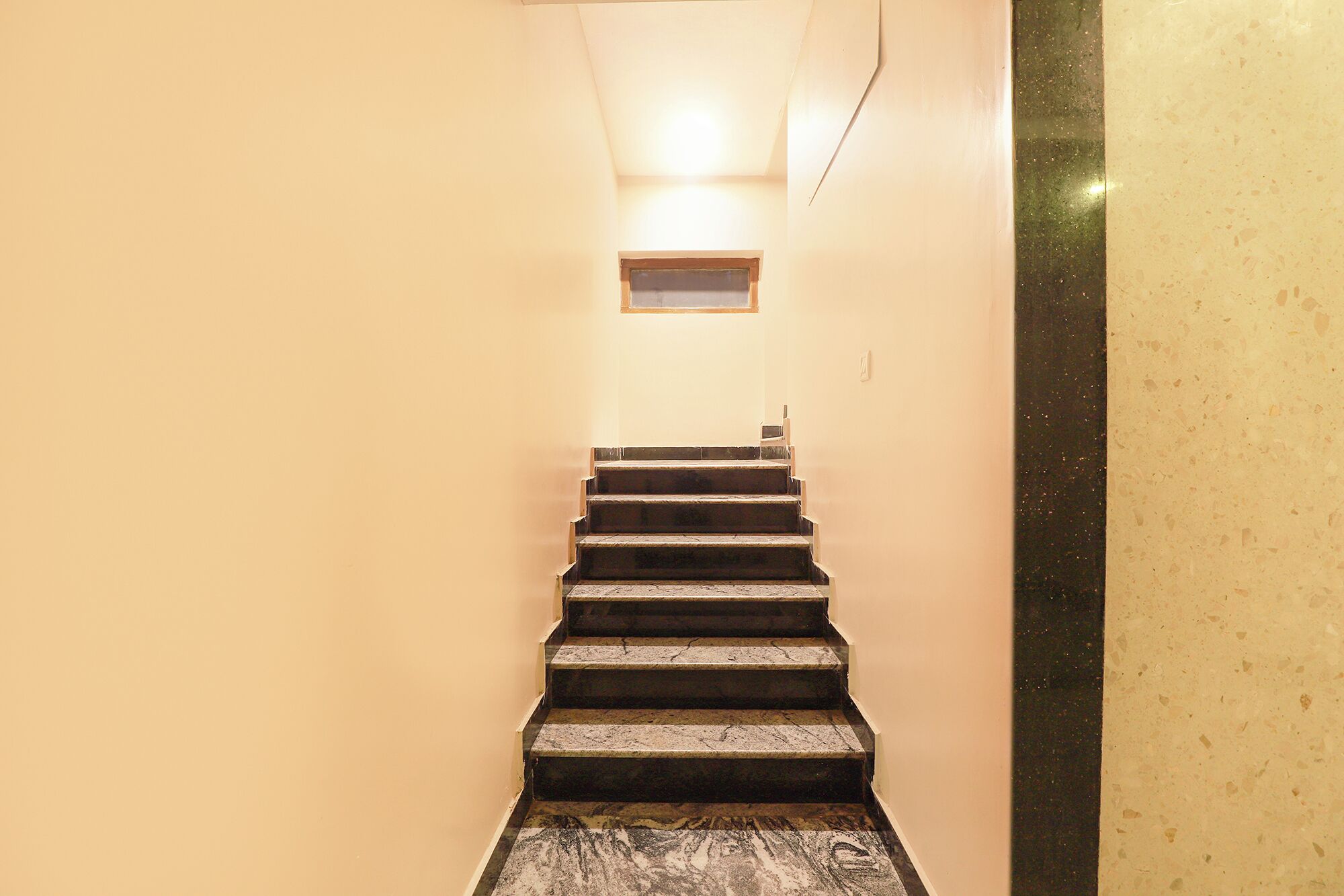 Eine enge Treppe mit Geländer auf der rechten Seite, die zu einer Zwischenebene mit einem kleinen Fenster führt.