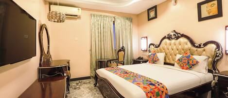 A hotel room with a large bed, a flat-screen TV, an air conditioning unit, a ceiling fan, a desk, and a chair.