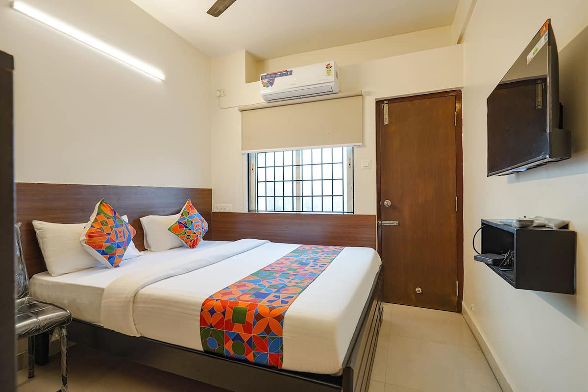 A hotel room with a bed, a window with bars, a TV mounted on the wall, and an air conditioning unit above the window.