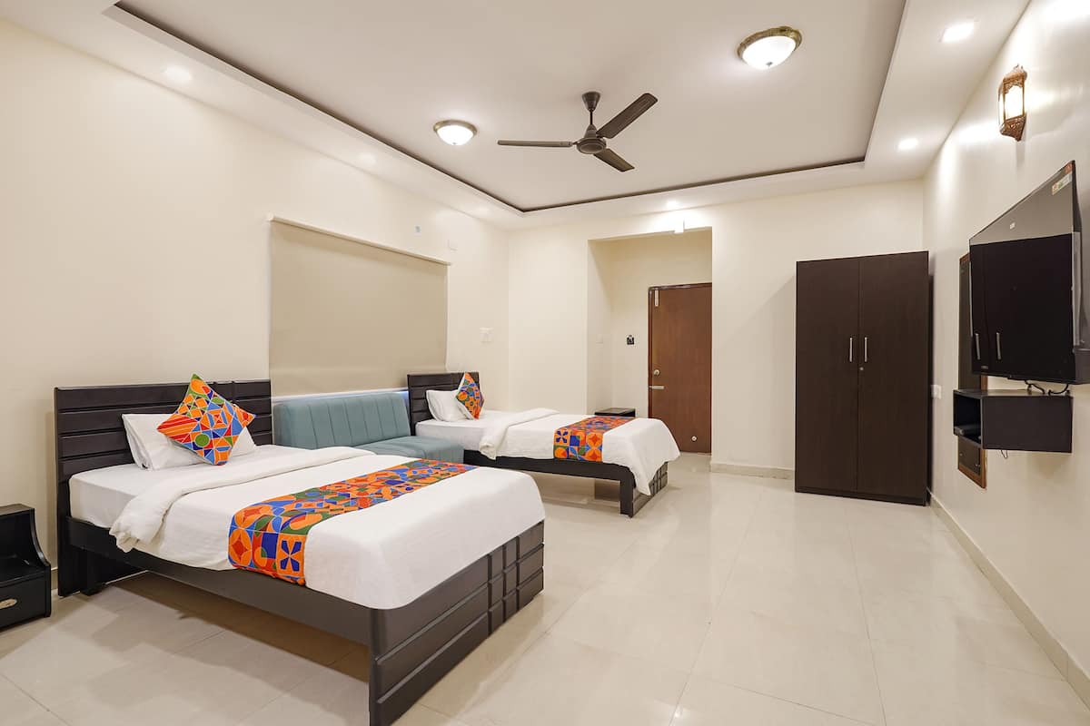 A hotel room with two beds, a ceiling fan, a TV mounted on the wall, and a wardrobe.