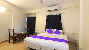 A hotel room with a bed, two chairs, a small table, and an air conditioning unit. - Fabhotel Devpriya (Chhatrapati Sambhajinagar)