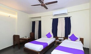 Habitación de hotel con dos camas, un escritorio, una silla, un ventilador de techo y un equipo de aire acondicionado.
