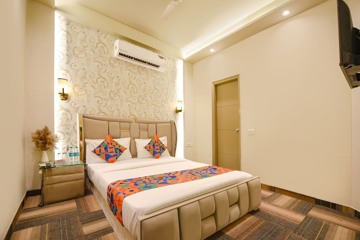 A hotel room with a large bed, a bedside table with a lamp, an air conditioning unit, and a door.