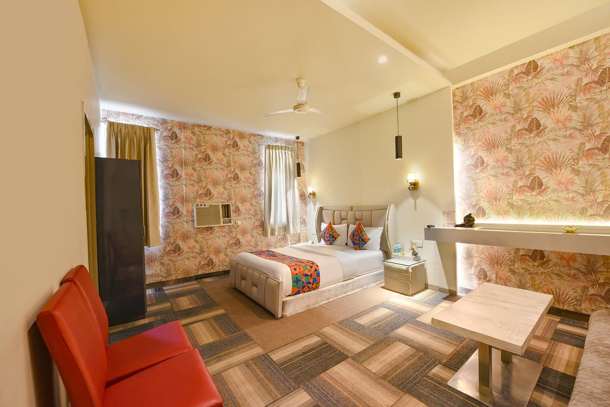 A hotel room with a bed, a desk, a chair, a ceiling fan, and a wall with floral wallpaper.