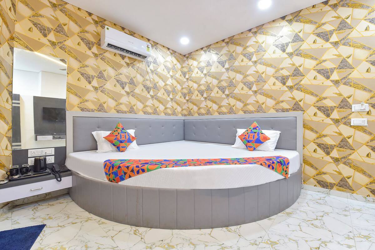 Une chambre à coucher moderne avec un lit aux lignes courbes, une tête de lit rembourrée de couleur grise et un papier peint à motifs.