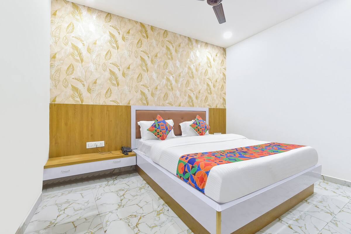 Une chambre moderne avec un sol en marbre, une tête de lit en bois, un lit agrémenté de coussins colorés et un ventilateur de plafond.
