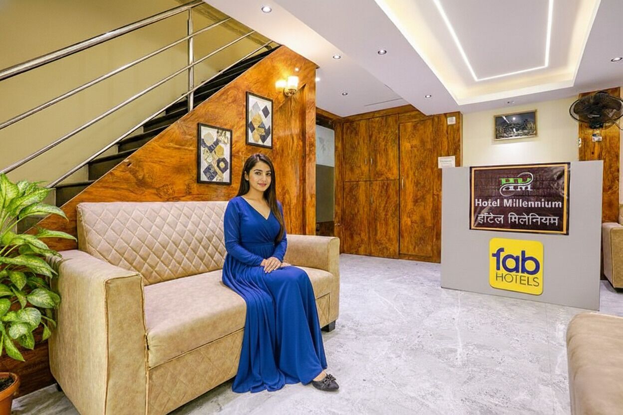 A hotel lobby with a staircase, a reception desk, and a person seated on a sofa.